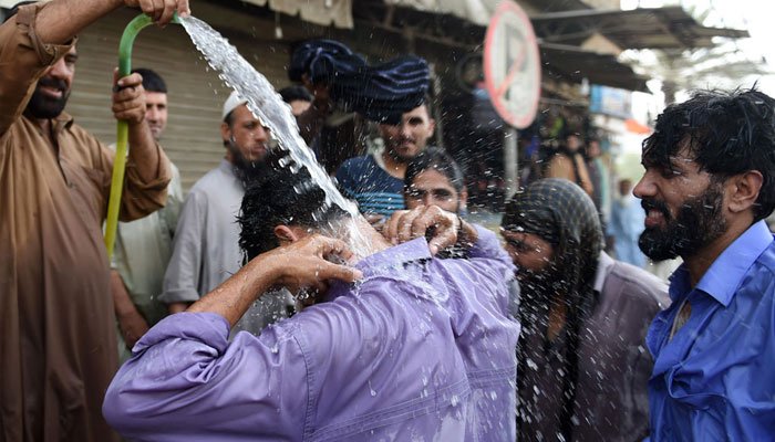 People walk under intense sunlight during hot and humid weather in Karachi.