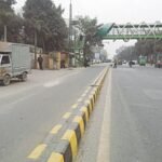 Pedestrians walk on a busy Karachi road after footpaths are blocked by encroachments and illegal parking.