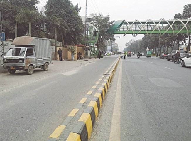 Pedestrians walk on a busy Karachi road after footpaths are blocked by encroachments and illegal parking.